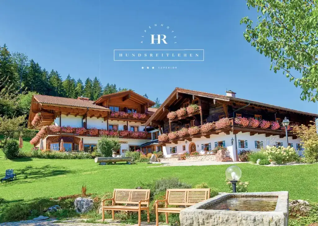 Hausprospekt Seite 1: Titel – das Alpenhotel Hundsreitlehen mit Blumenbalkonen, Brunnen und Bergwiese